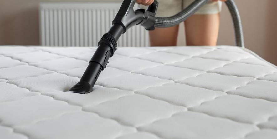 Person using a vacuum cleaner on a clean, white mattress during a professional mattress cleaning service.