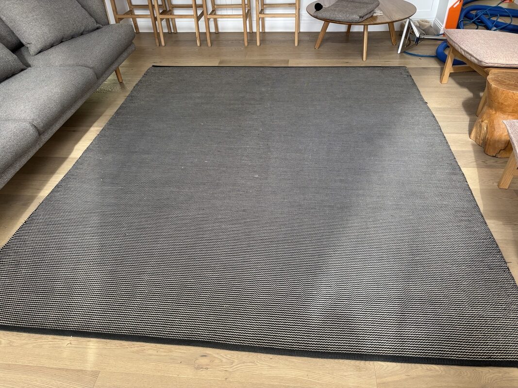 Freshly cleaned area rug on hardwood floor, showcasing revitalized texture and appearance, adjacent to a modern sofa and dining area, highlighting the transformative effects of professional cleaning services by Exceed Carpet Cleaning.