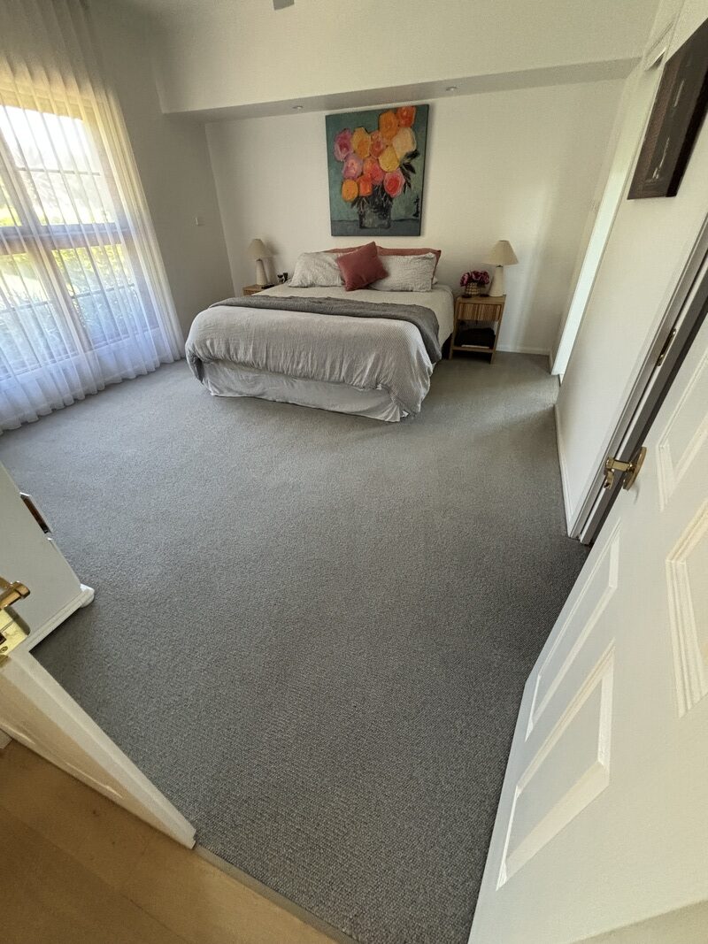 Clean and refreshed bedroom with a neatly made bed, decorative pillows, and a colorful floral painting, showcasing revitalized carpet and inviting atmosphere after professional cleaning by Exceed Carpet Cleaning.