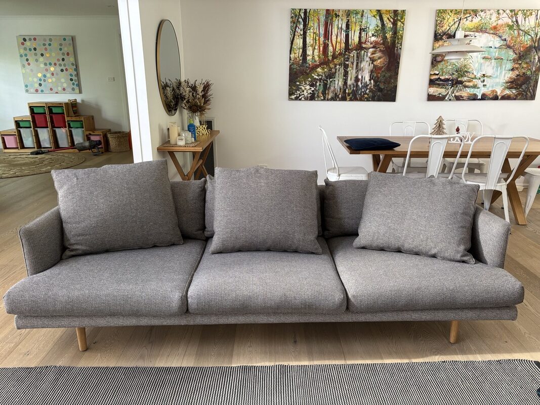Gray sofa with plush cushions in a bright, modern living room featuring artwork on the walls, a dining table, and colorful storage bins, illustrating a clean and inviting home environment after professional cleaning by Exceed Carpet Cleaning.