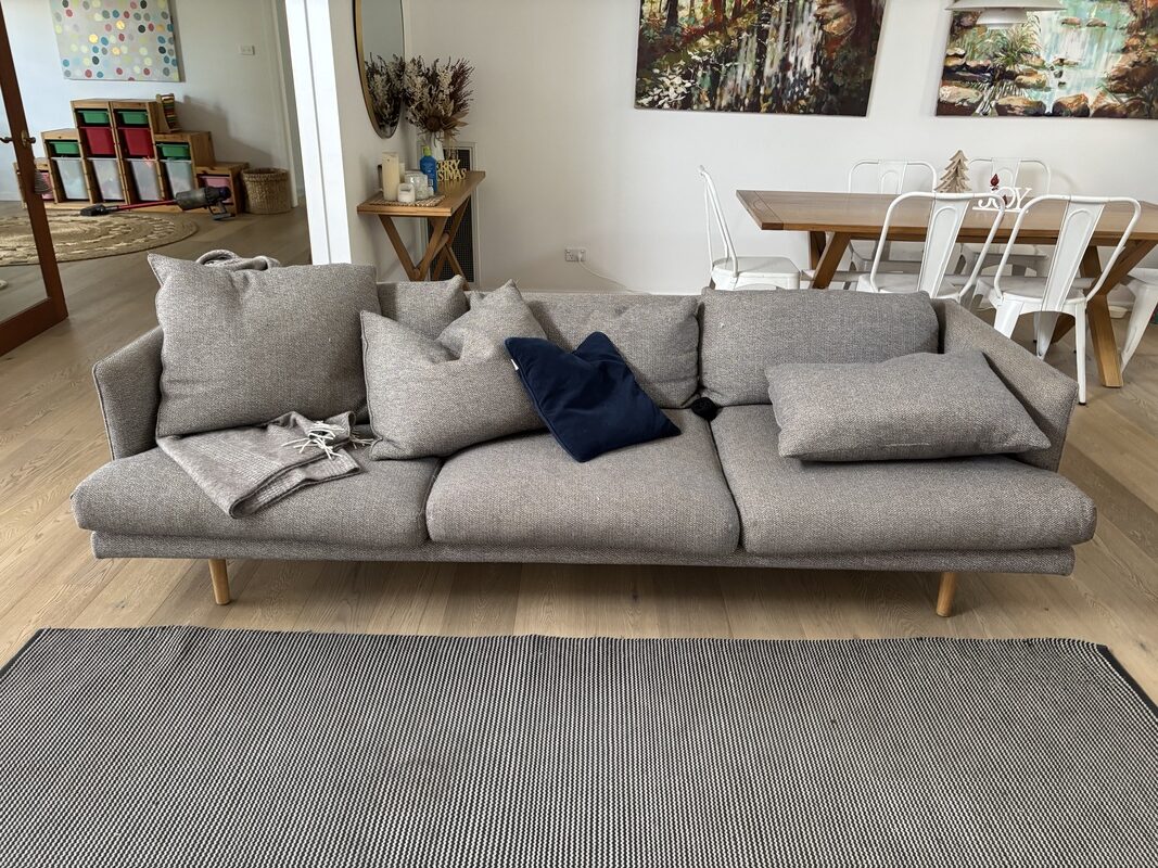 Sofa with scattered cushions and a throw blanket, in a family living room setting, highlighting the need for professional upholstery cleaning before holiday gatherings.